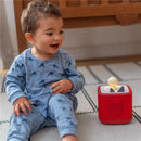 A smiling toddler in blue pajamas sits cross-legged next to a red Tonies Sleepy Duck audio toy, which features a small duck figurine.
