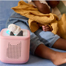 Tonies Sleepy Friends audio player in pink with a sheep figurine, featuring lullaby melodies, near a child resting on a blue surface.