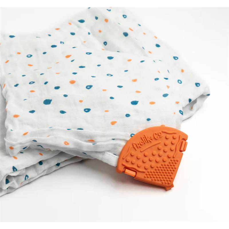 Teether clip in papaya color attached to a patterned muslin fabric with blue and orange dots.