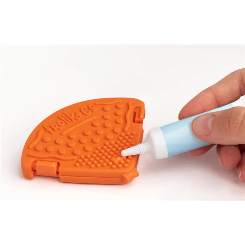 Teether clip in papaya color being filled with a liquid from a small blue applicator.