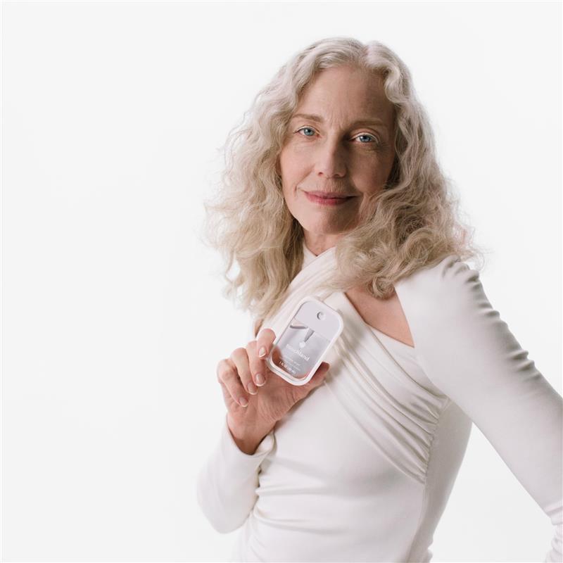 Woman with curly hair wearing a white top, holding a Touchland Hand Sanitizer Mist in a silicone case, Icy White.