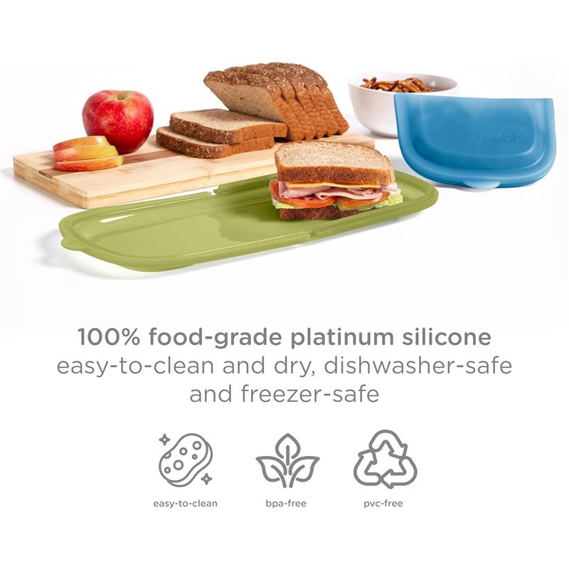 Reusable silicone storage bags in olive and juniper colors on a table with bread, apple slices, and a bowl of snacks.