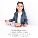 A smiling girl holds a purple silicone storage bag with apple slices and a sandwich, showcasing its use for mealtime.