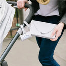 Retractable on-the-go bag dispenser for travel, attached to a stroller, held by a person wearing a gray shawl.