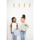 Two kids smile at each other while holding colorful bento lunch boxes; one is sage green and the other light blue.