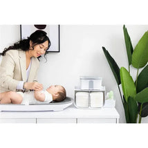 Caddy organizer by Ubbi holds baby diapers and wipes next to a mother changing her infant on a changing table.
