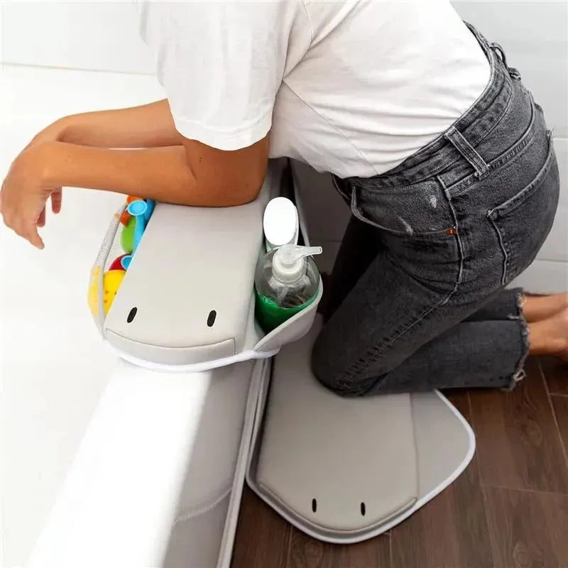 Cushioned gray elbow rest with compartments for bath toys and hand soap, used by a person kneeling next to a bathtub.