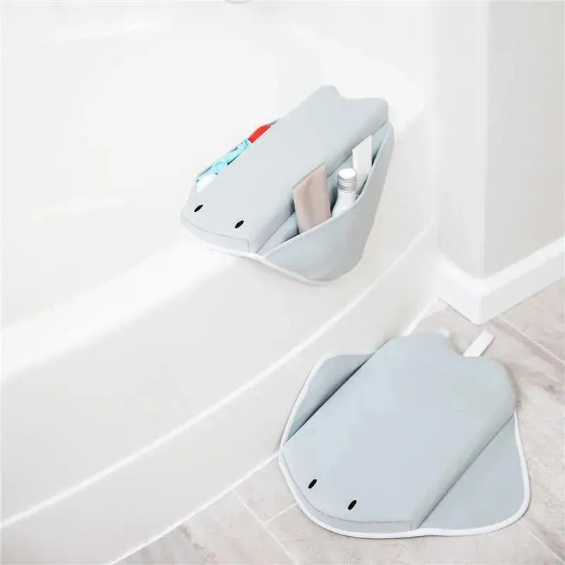 Cushioned gray stingray-shaped elbow rest positioned on a bathtub edge, holding personal care items.