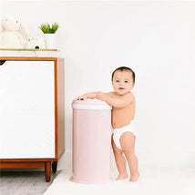 Blush pink Ubbi Steel Odor Locking Diaper Pail next to a smiling baby in a diaper against a white background.