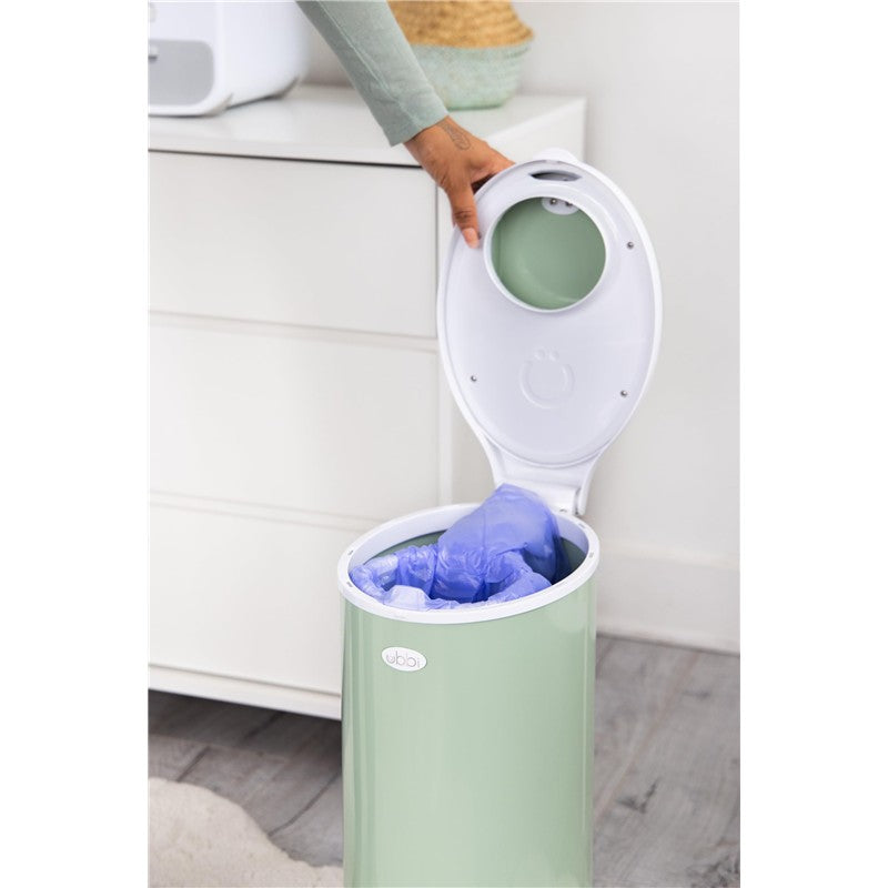 Ubbi diaper pail with open lid, containing blue disposable bags inside, set on a wooden floor.