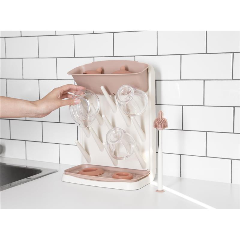 Vertical drying rack with glass storage, featuring a pink top, multiple drying pegs, and a bottle cleaning brush on a countertop.