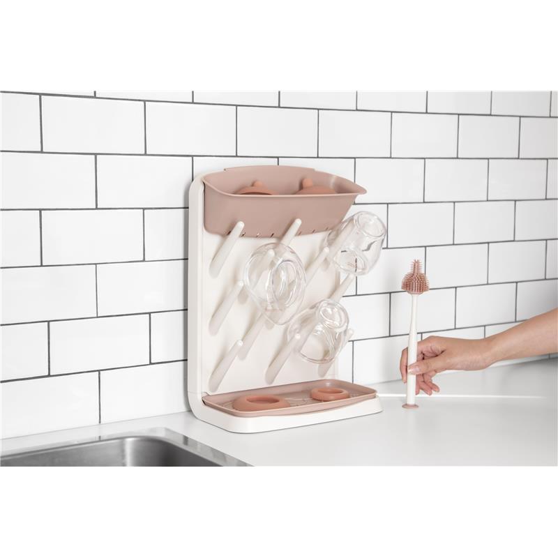 Vertical drying rack for bottles and accessories with a beige and pink design, featuring glasses and a cleaning brush nearby.
