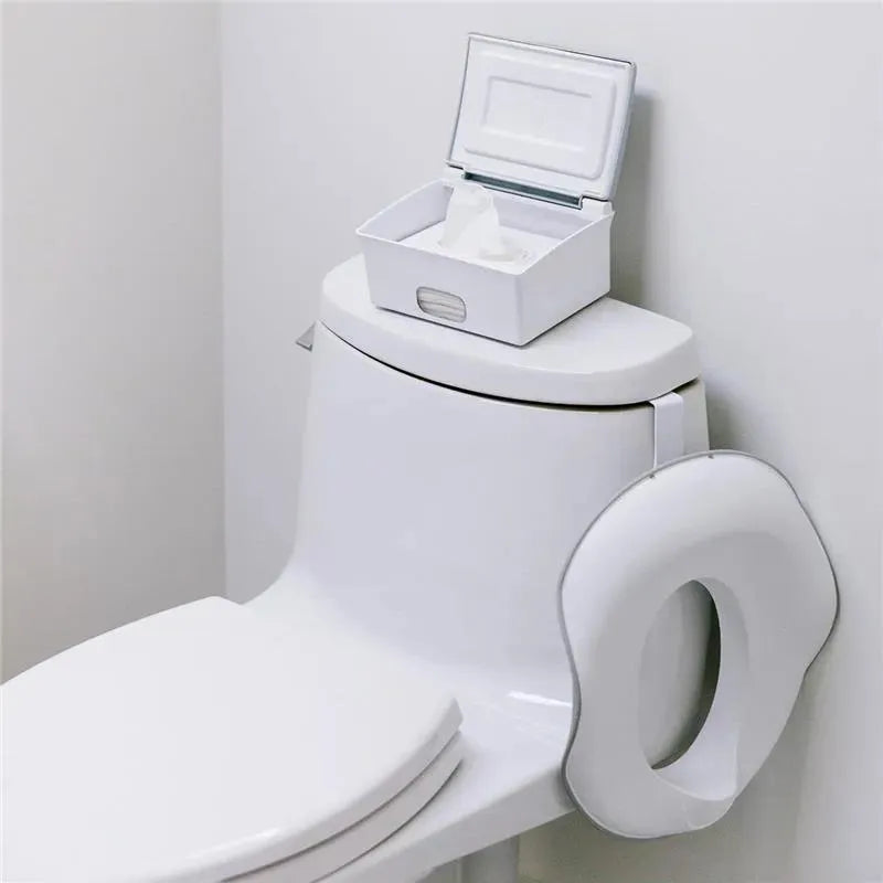 Ubbi flushable wipes dispenser in white and grey placed on a white toilet seat.