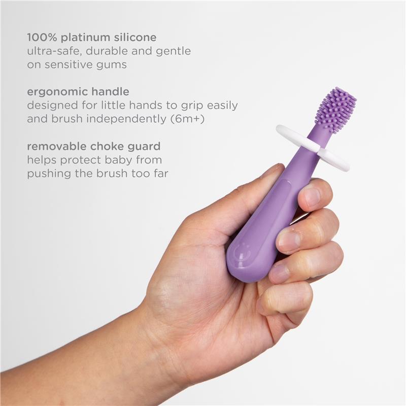 Purple silicone toothbrush for babies, featuring an ergonomic handle and removable choke guard, held in a hand.