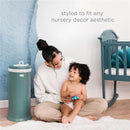 Steel diaper pail by Ubbi in green, placed beside a mother playing with her toddler in a nursery setting.