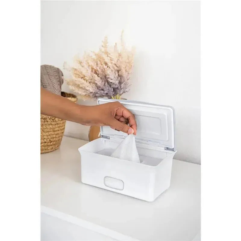 Gray Ubbi baby wipes dispenser with a hand pulling out a wipe, set against a light background adorned with dried flowers.