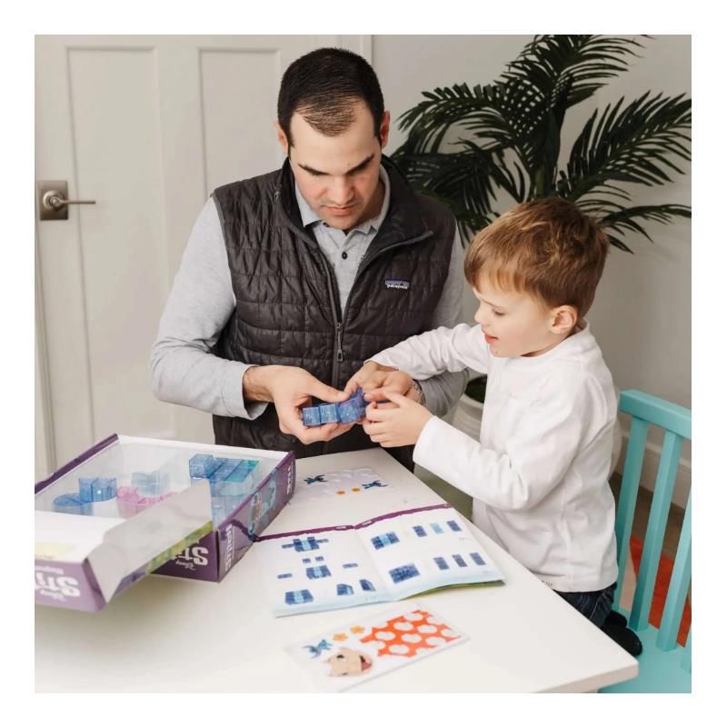 A man and a child engage with the United Pacific Designs Tytan Disney Stitch 53 Piece Cube Magnetic Tile Kit, assembling blue magnetic tiles while a guidebook is visible.