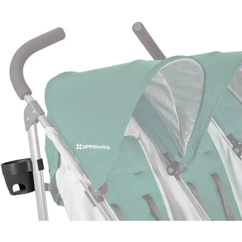 Uppababy cup holder attached to a stroller handle, designed for G-Link/G-Luxe models, with a teal canopy in the background.