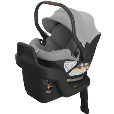 Uppababy Aria Infant Car Seat in Light Grey, featuring adjustable handle, protective canopy, and safety labels on the base.