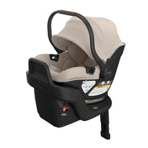 Uppababy Aria V2 infant car seat in Sandstone Melange with Chestnut Leather handle, featuring safety stickers and a reclining position.