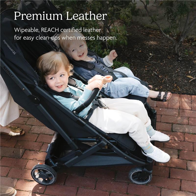 Dual children seated in the UPPAbaby Minu Duo stroller, featuring premium leather seats and a chestnut bumper bar.