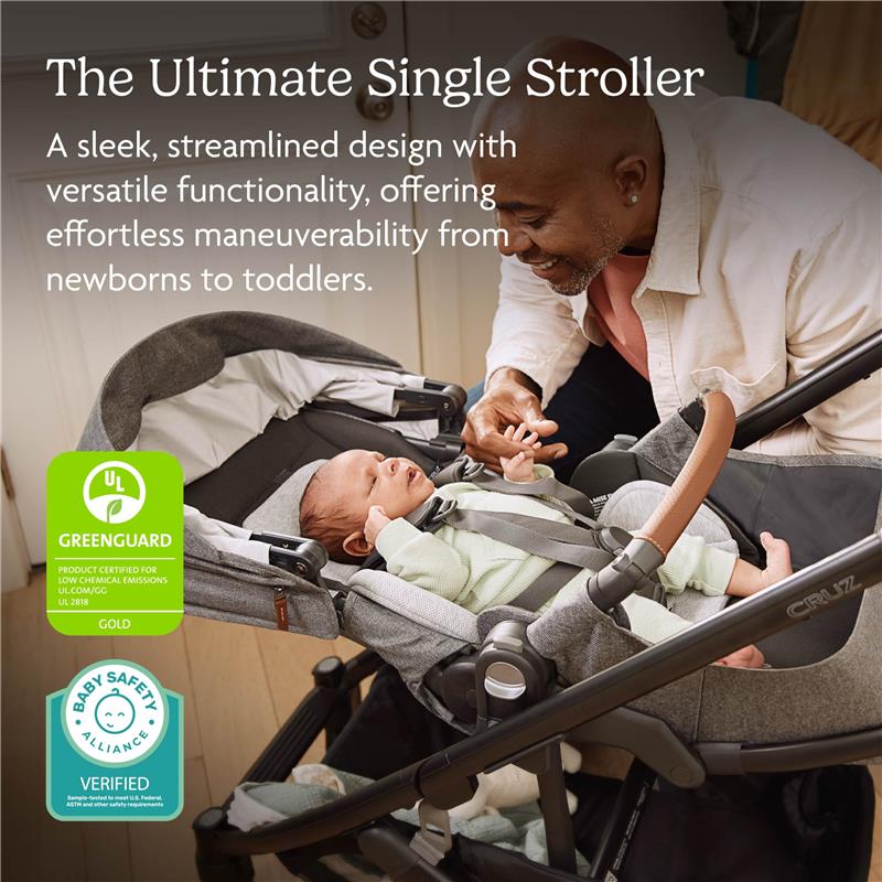 Uppababy Cruz V3 stroller in Meadow Green with a graphite frame and chestnut leather, featuring a baby securely strapped inside and a smiling adult interacting.