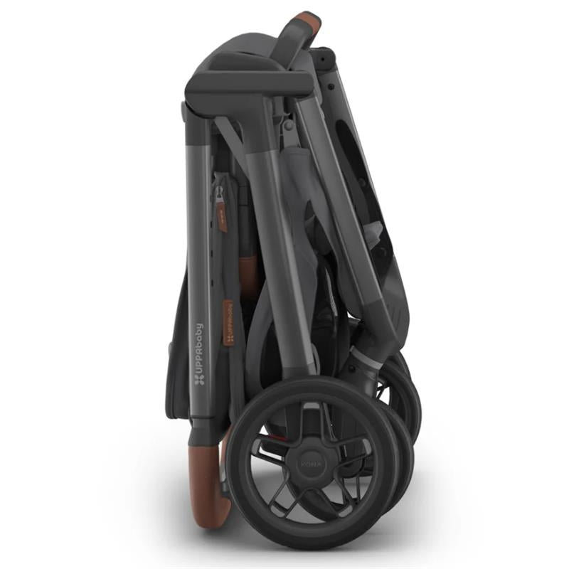 Uppababy Kona Stroller in a folded position, featuring sleek grey fabric and brown leather accents on the handle.
