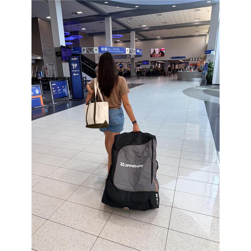 A woman walking in an airport, pulling an UPPAbaby travel bag for Vista and Cruz strollers.