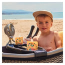 Portable fan attached to a baby stroller, with a shirtless boy sitting on the beach, enjoying snacks from pouches.