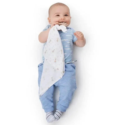 Baby smiling and holding a soft, patterned swaddle over denim-like pants, showcasing comfort and playfulness.