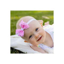 Light pink elastic baby headbands with gingham bows worn by a smiling baby girl on a blanket outdoors.