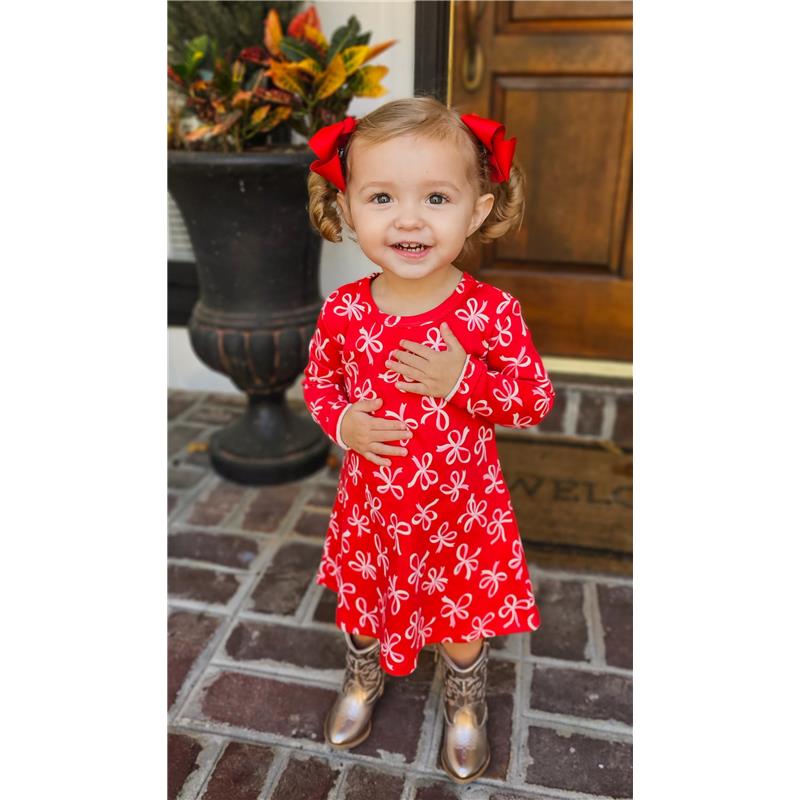 Baby girl wearing a red dress with white bows, smiling and posing, accented with two red grosgrain hair bows.