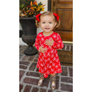 Baby girl wearing a red dress with white bows, smiling and posing, accented with two red grosgrain hair bows.