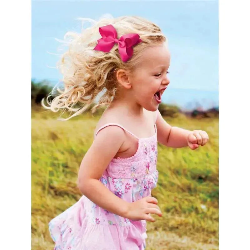 A young girl with curly blonde hair wearing a pink dress and a pink satin hair bow is joyfully running outdoors.
