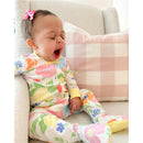 A young child yawning while sitting in a cozy chair, wearing a floral-patterned, colorful outfit.