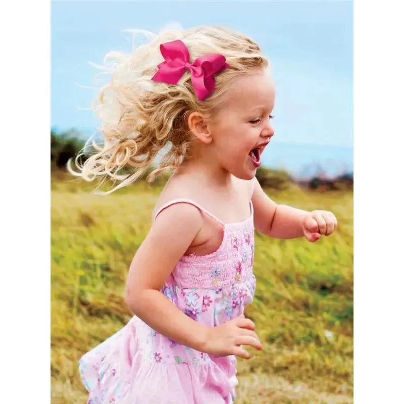 Young child with curly hair wearing a pink dress and a large pink bow, joyfully running outdoors.