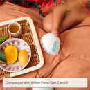 Willow 360 reusable breast milk container with a teal button, placed beside mangoes and a cup on a tray.