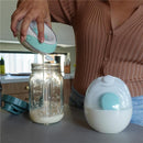 A person is pouring liquid from a light blue Willow Go Container Kit into a clear glass jar on a countertop.