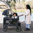 Wonderfold W4 Series Car Seat Adapter attached to a stroller with a child smiling inside, while a parent stands beside them.