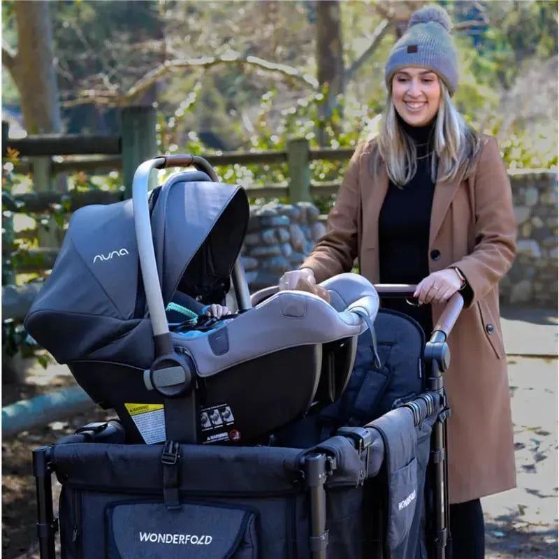 Wonderfold W4 Series Car Seat Adapter with a Nuna infant car seat in a stroller, pushed by a smiling woman in a tan coat and hat.
