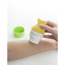 Yellow fish tail-shaped sunscreen applicator being used on an arm with a green container beside it.