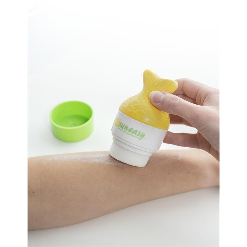 Yellow fish tail sunscreen applicator being used on a tanned arm, with a green cap in the background.