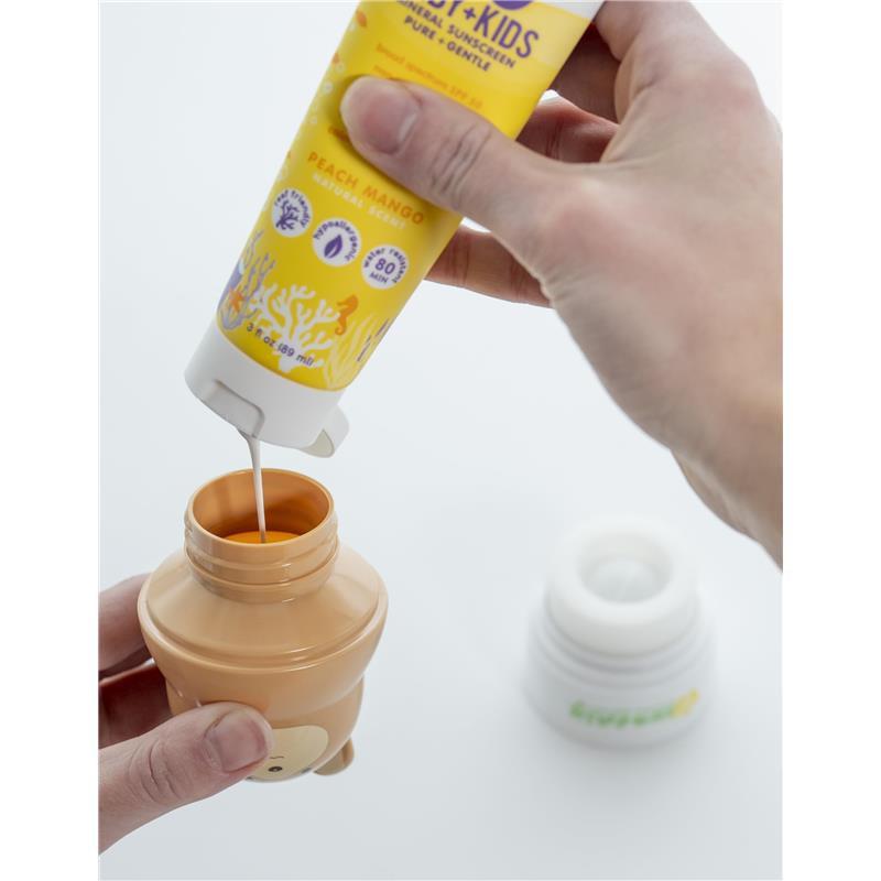 Hand pouring peach mango sunscreen from a yellow tube into a teddy bear-shaped applicator.