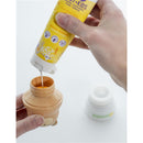 Hand pouring peach mango sunscreen from a yellow tube into a teddy bear-shaped applicator.