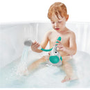 A toddler plays with a green Yookidoo elephant bath shower head, using its trunk spout rinser in a tub filled with water.