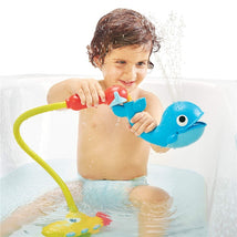 A child in a bathtub plays with the Yookidoo Submarine Spray Whale, which squirts water, enhancing bath time fun.