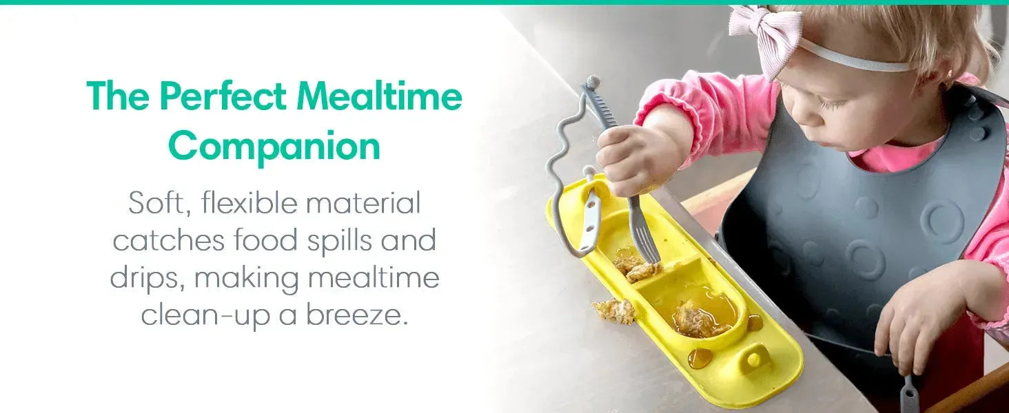 Baby using yellow silicone catch-all tray with fork, wearing gray bib during mealtime