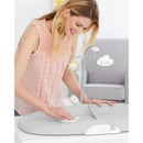 A woman wipes a grey Skip Hop wipe-clean changing pad, which features a toy mobile with a sun and cloud, in a nursery setting.
