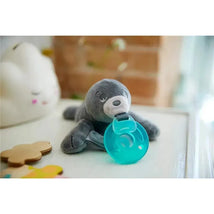 Soft gray seal plush with a teal pacifier attached, surrounded by colorful toys on a white surface.