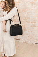 JuJuBe Insulated Bottle Bag in black, held by a woman in a cream dress, with a child smiling in her arms.